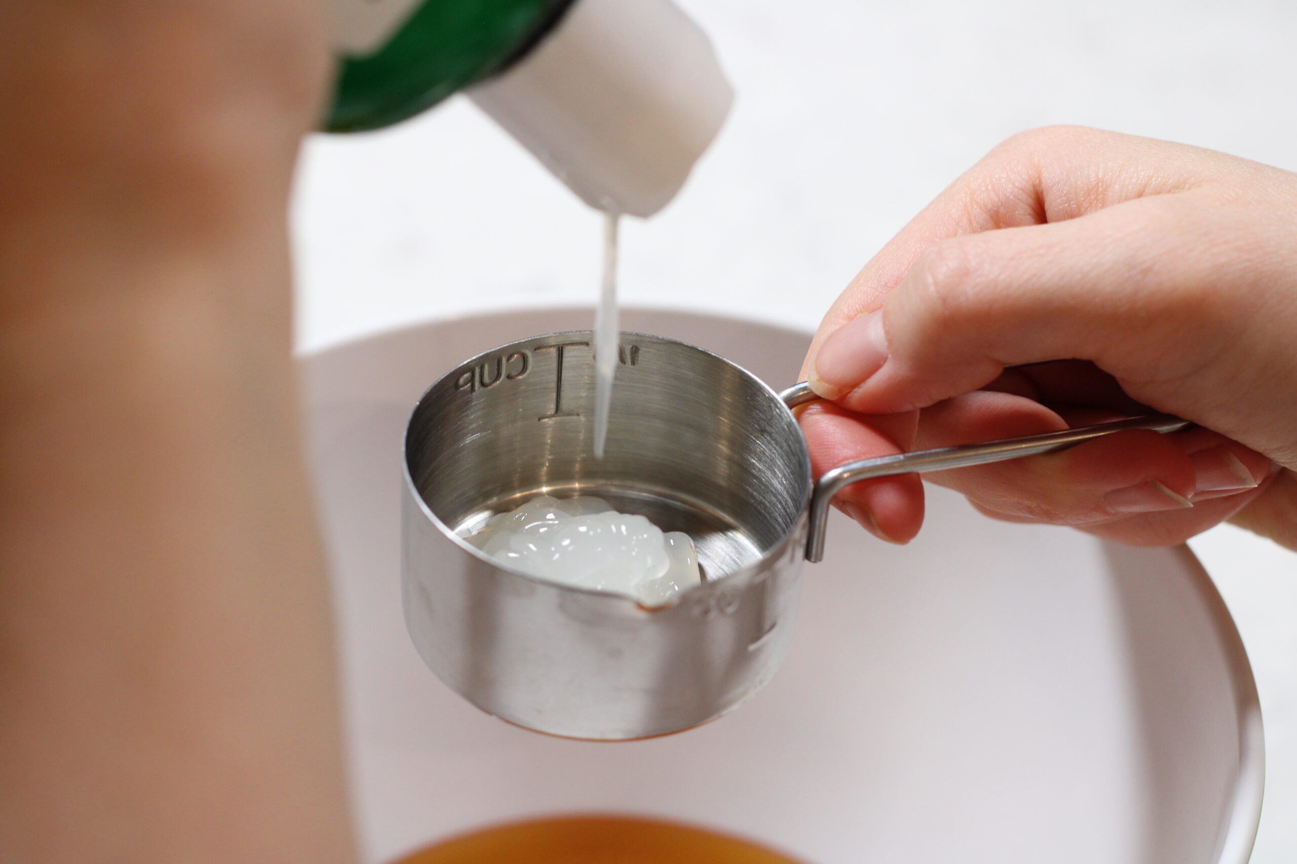 a hand pouring aloe vera into a measuring cup