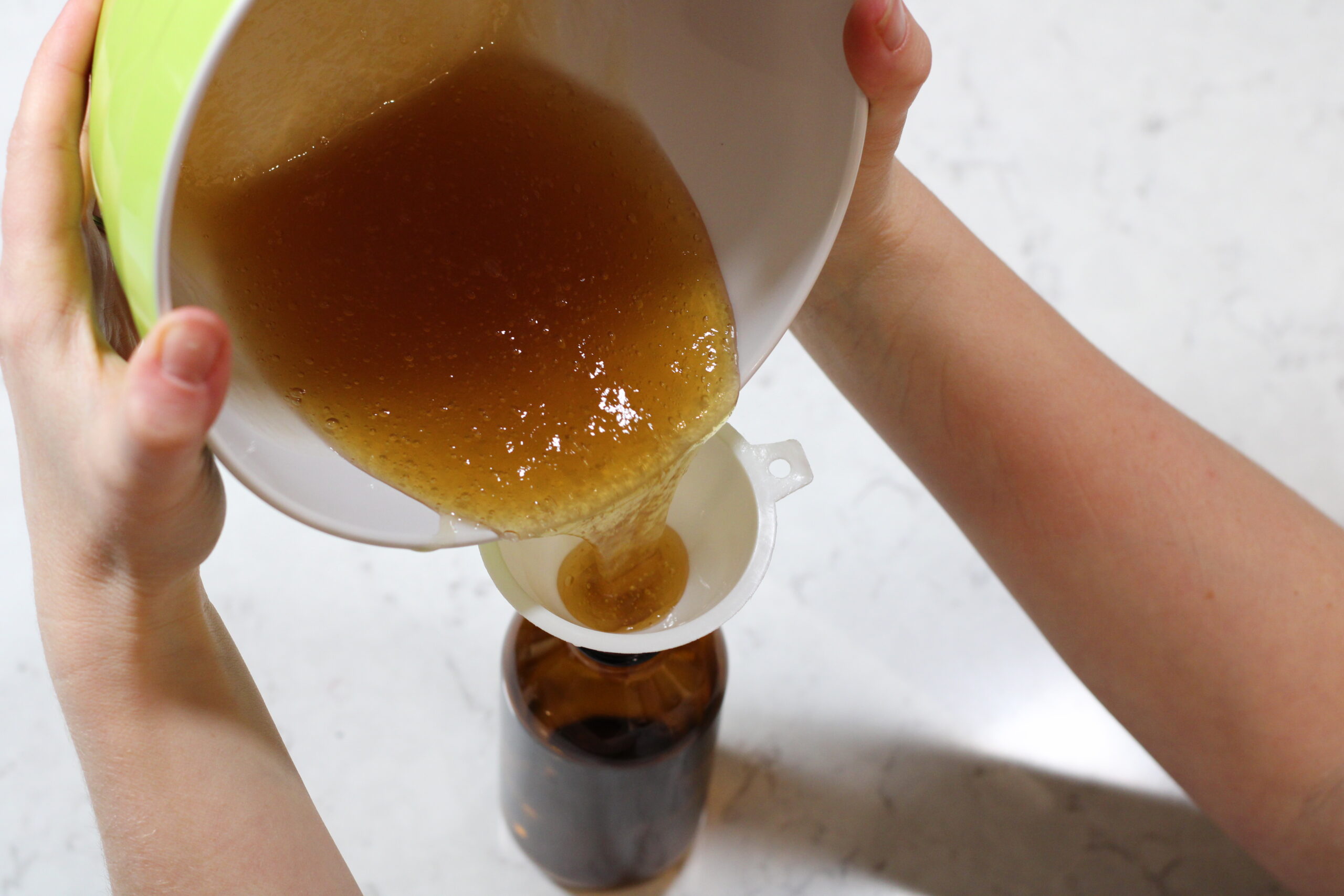 honey face wash being poured from a bowl into a funnel and glass bottle