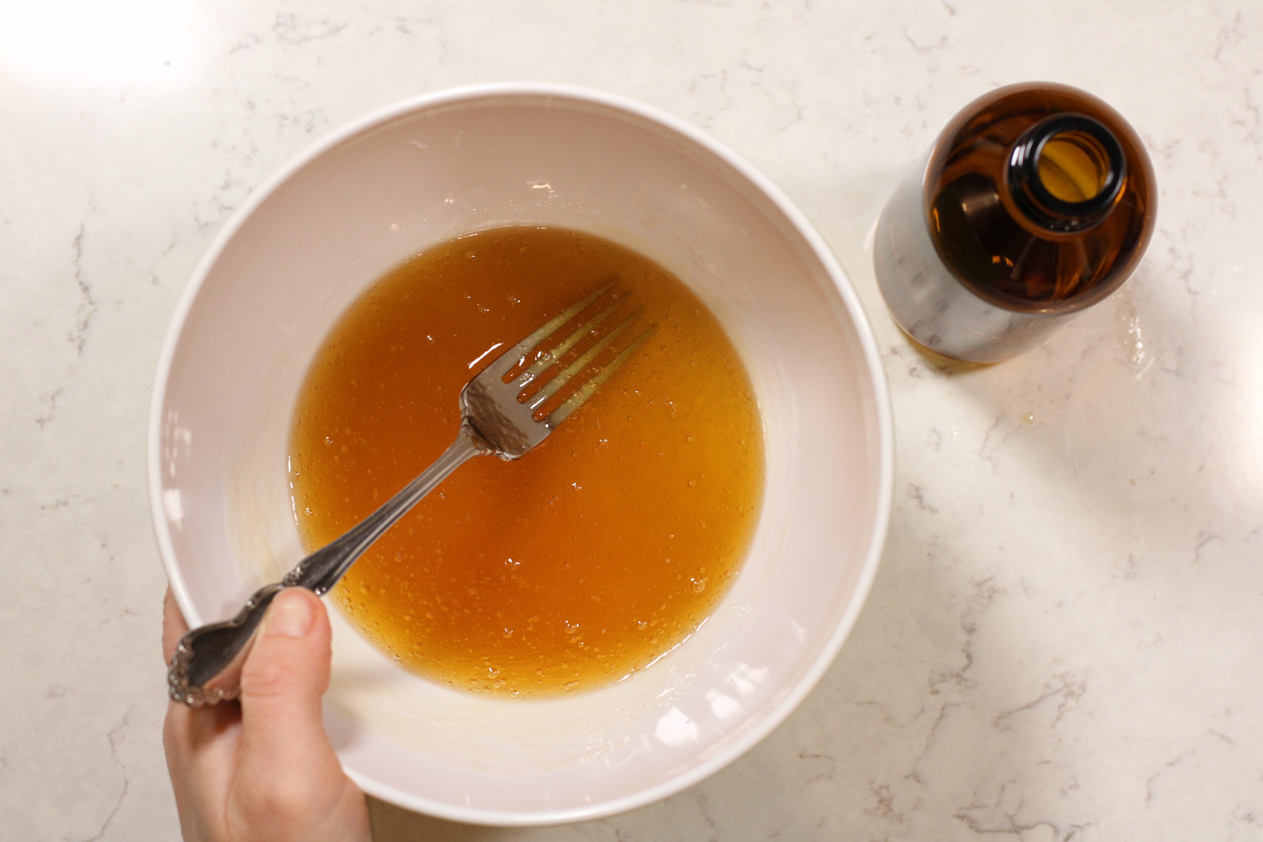 honey face wash in a mixing bowl next to glass bottle