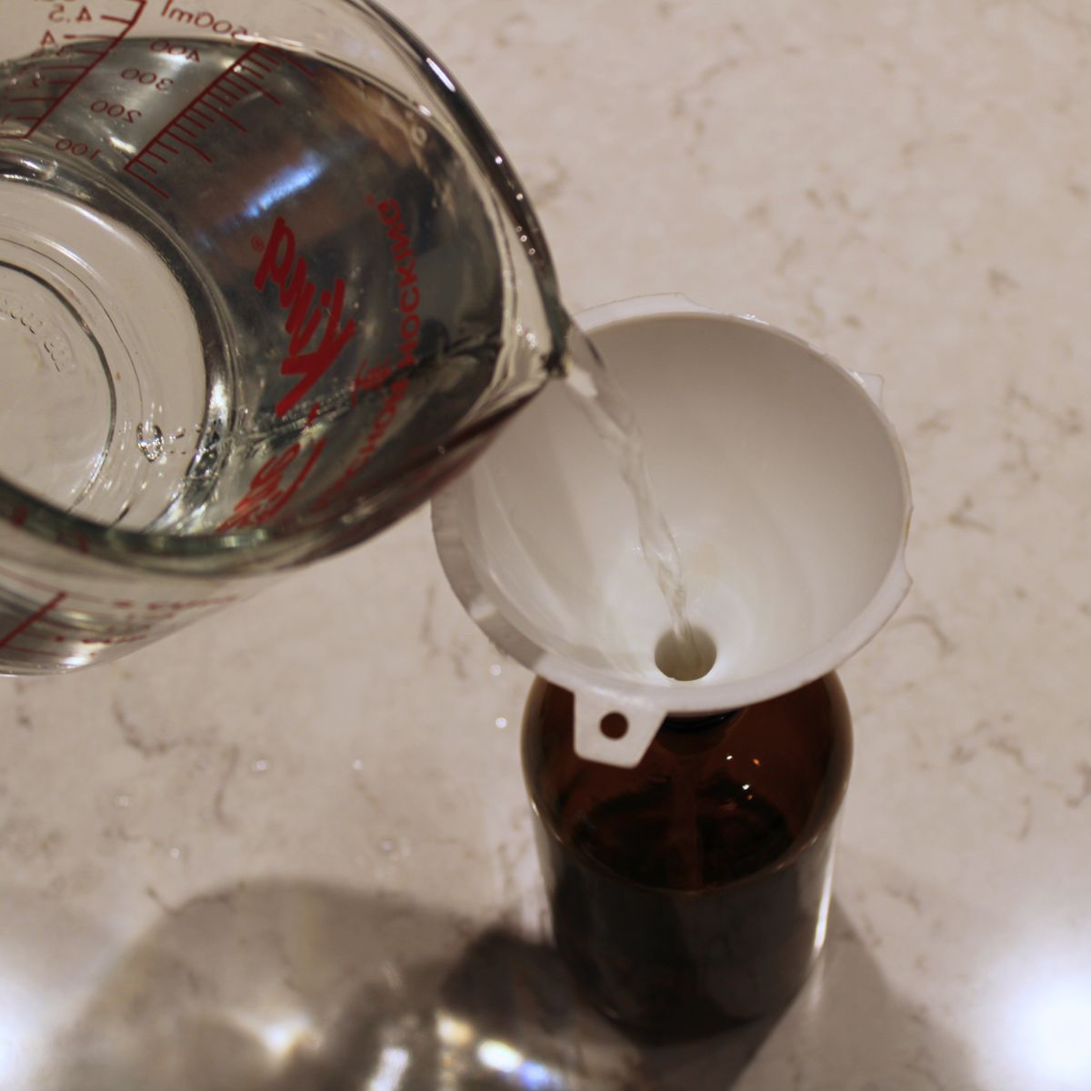 liquid being poured from measuring cup through a funnel to a bottle