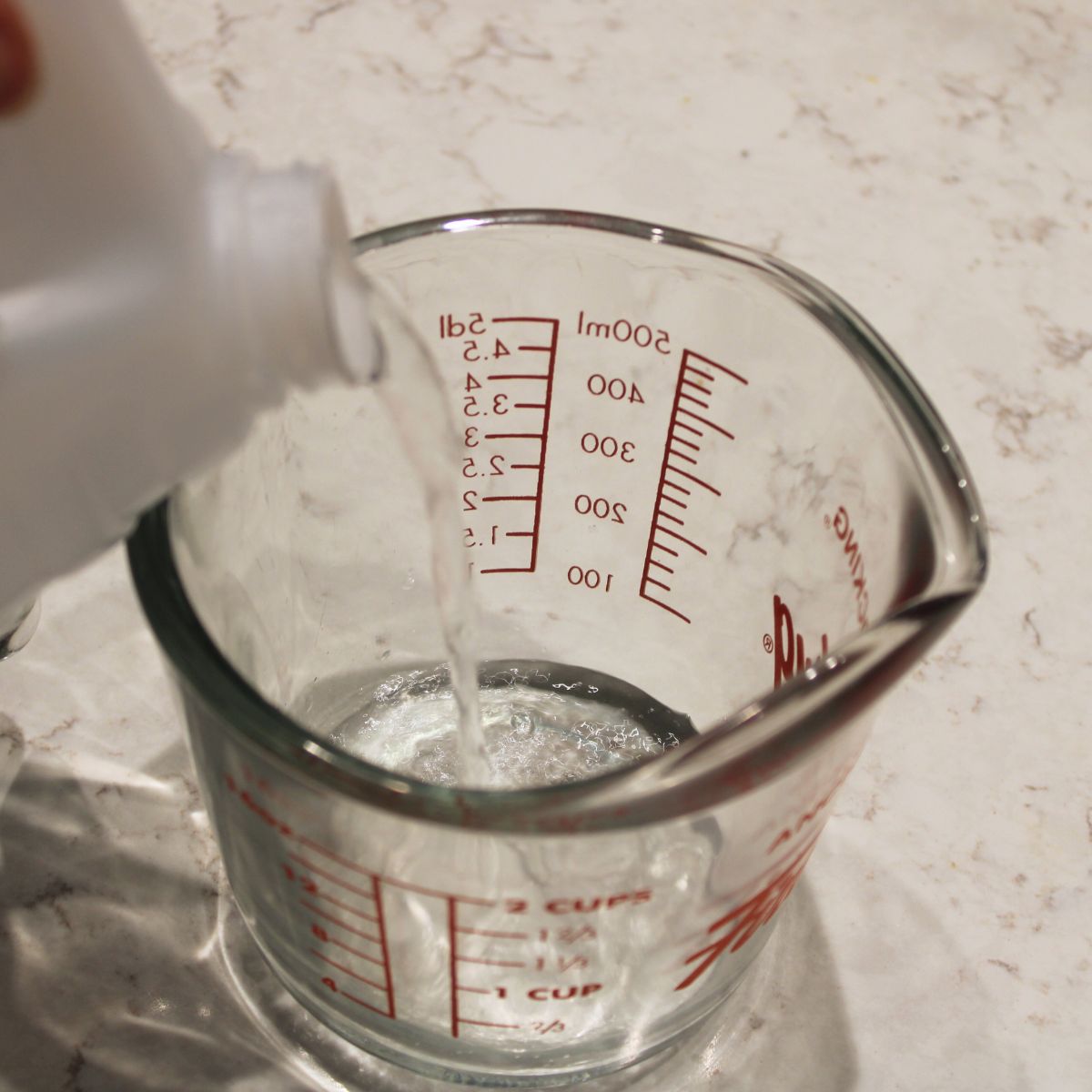 vinegar being poured into a glass measuring cup