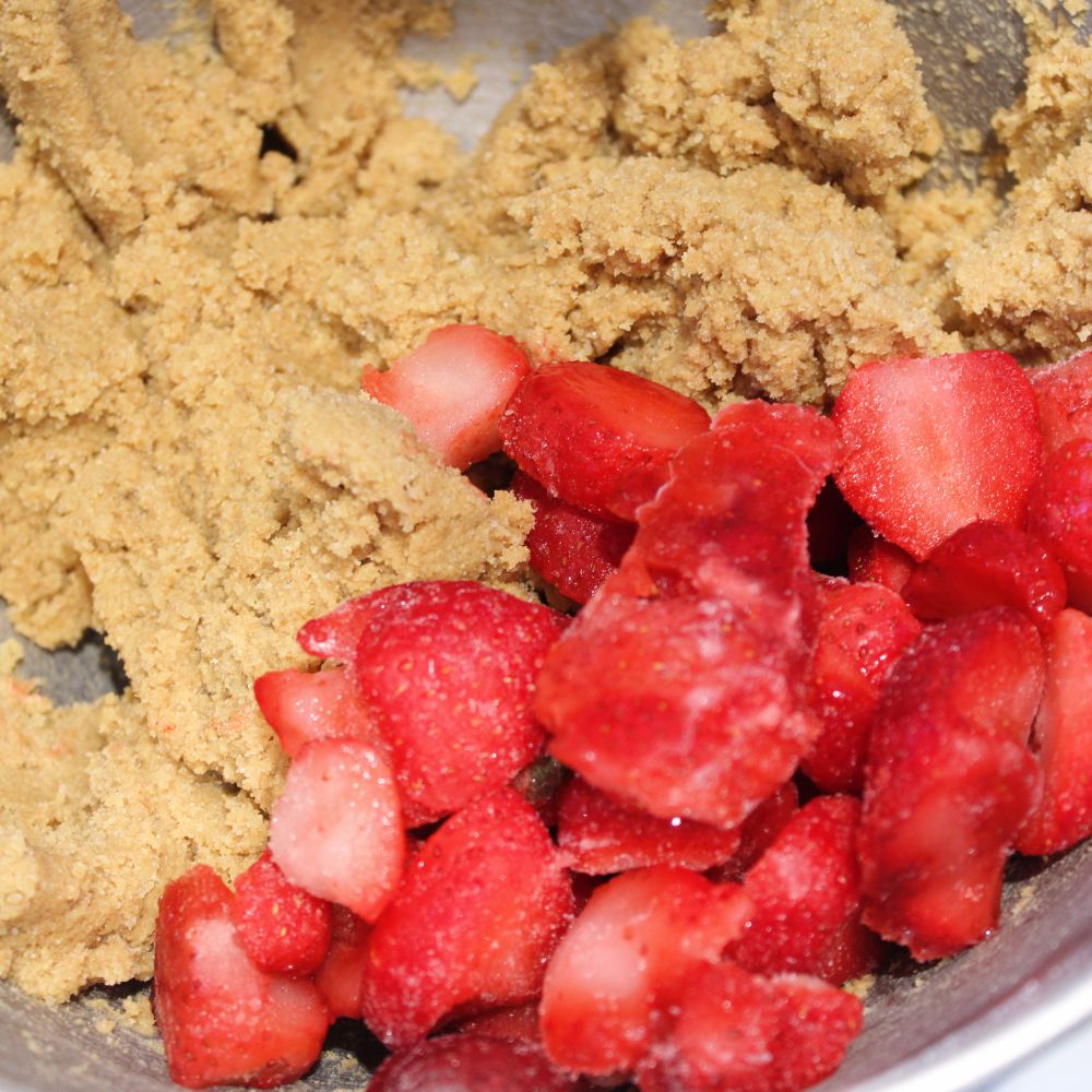 frozen strawberries on top of dough in the bowl of a stand mixer