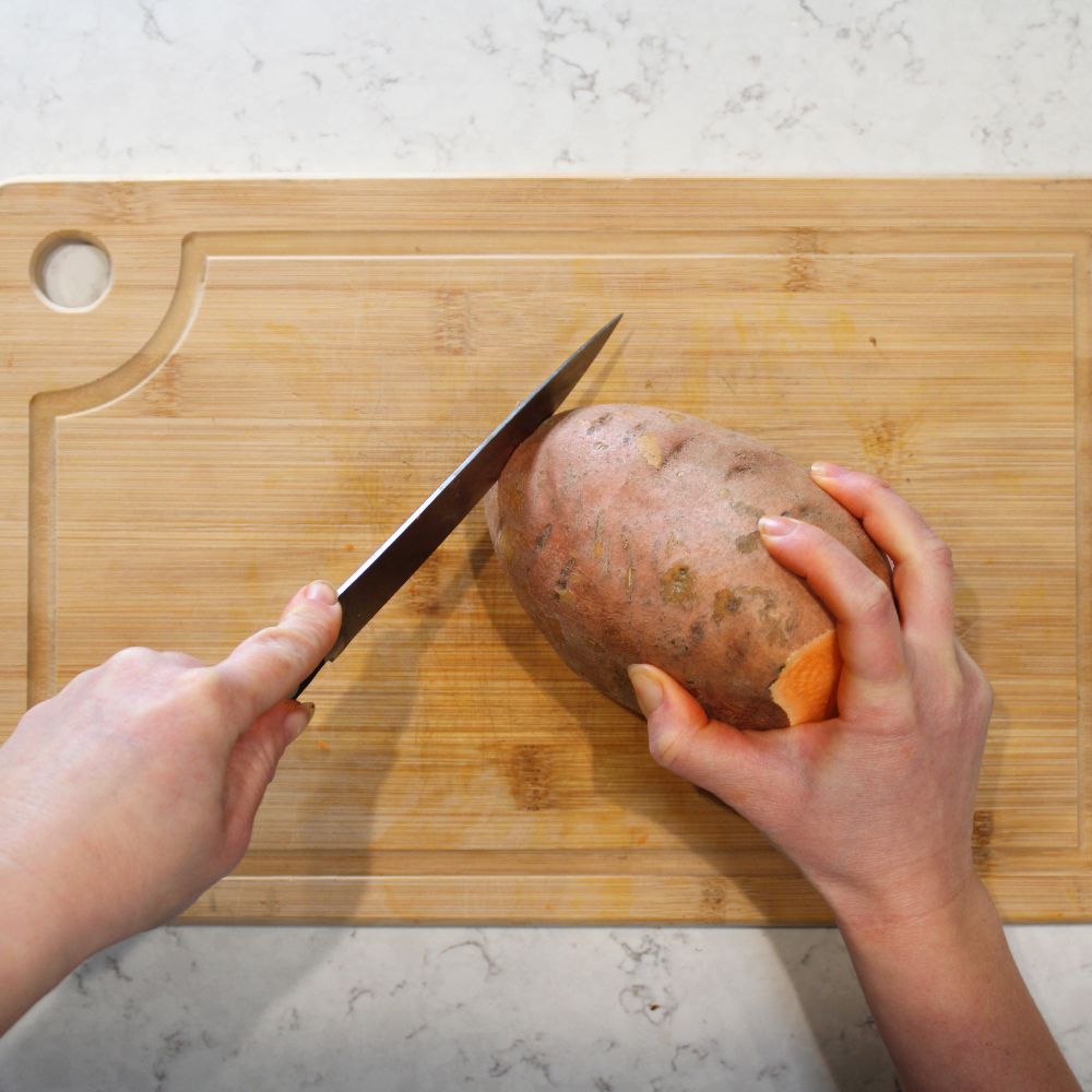 hand cutting a sweet potato on a wood cutting board