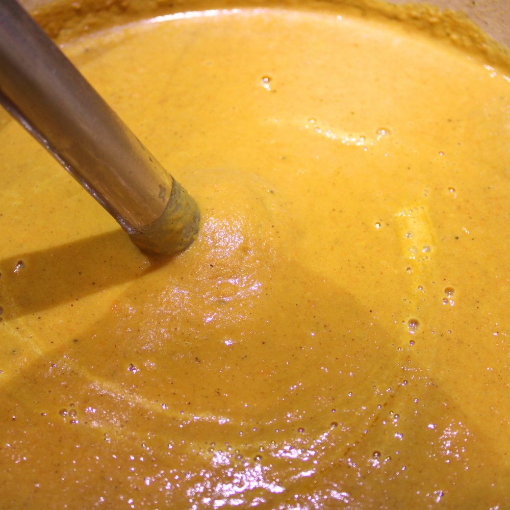 close up of soup in a pot being blended by an immersion blender