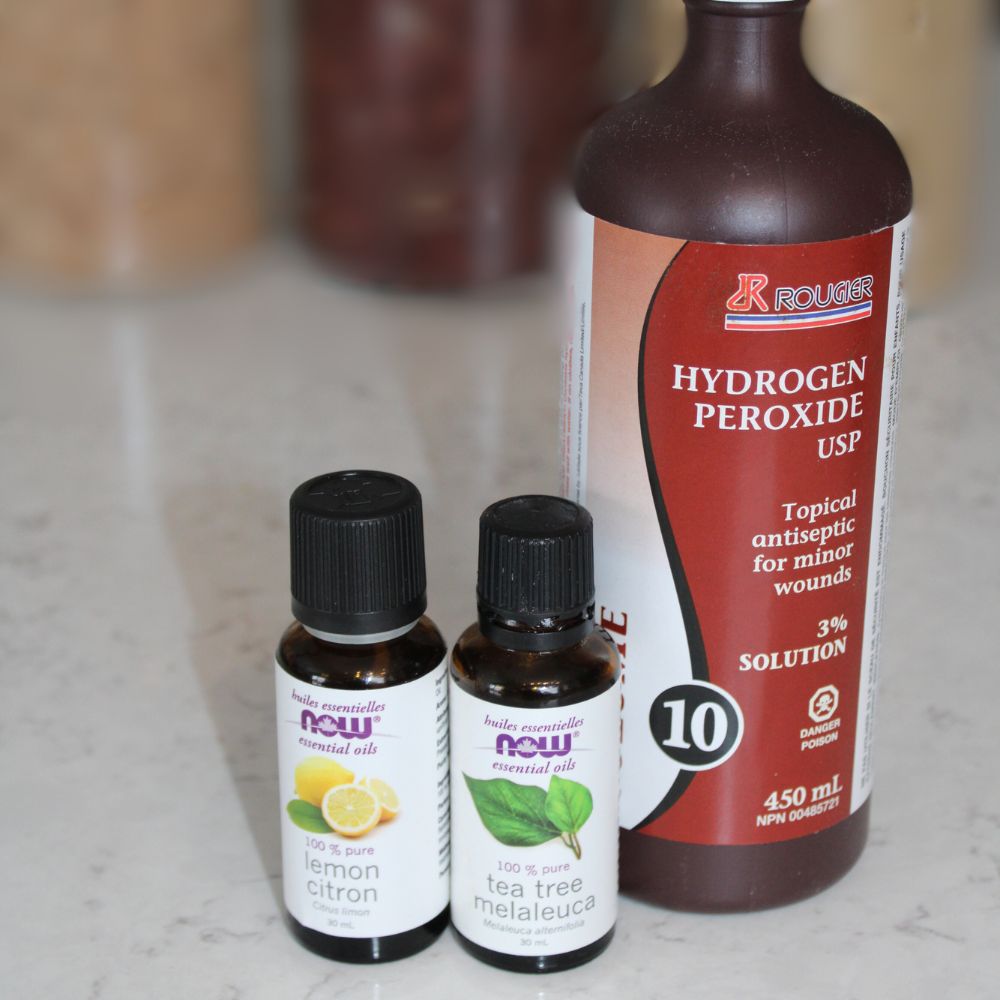 bottle of hydrogen peroxide with tea tree and lemon essential oil bottles