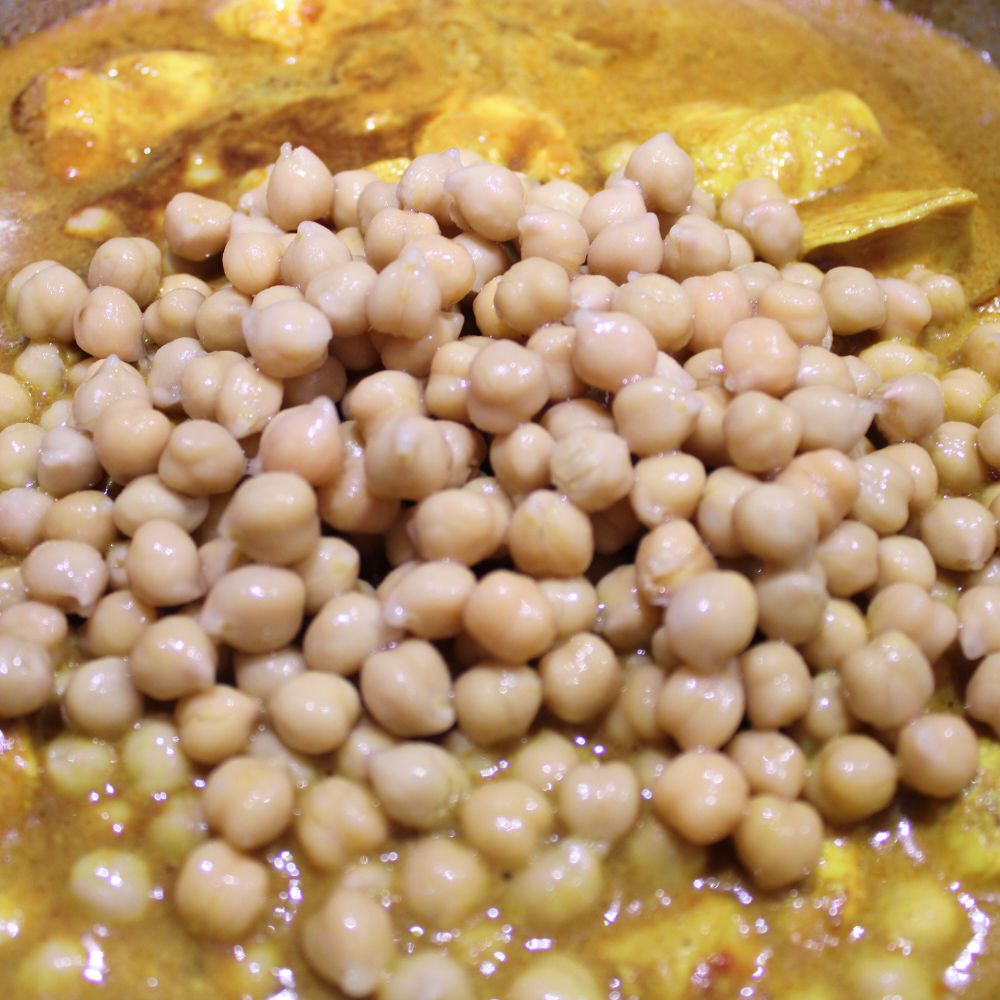 close up of chick peas poured over marinated chicken cooking in a pot