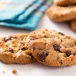 close up of two chocolate chip cookies with a tea towel in the background