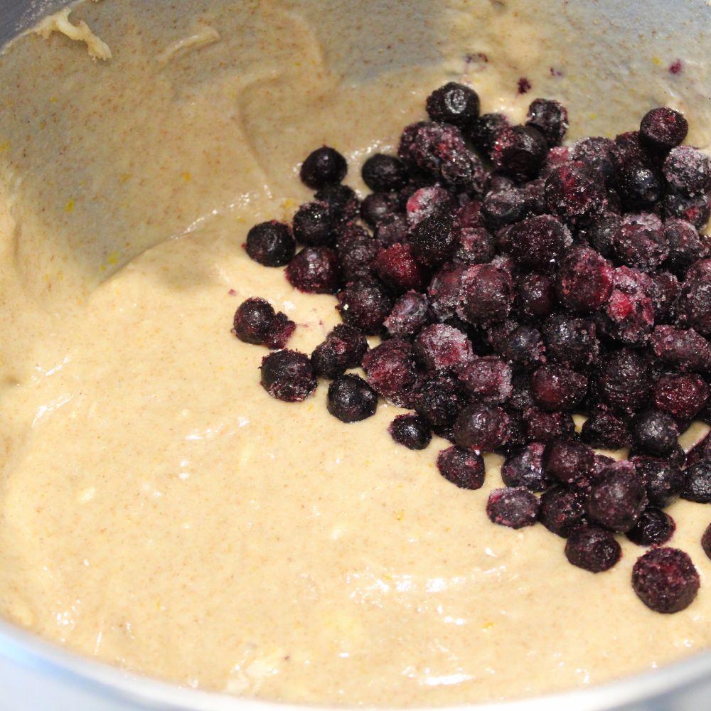 muffin batter in a mixing bowl with frozen blueberries poured on top