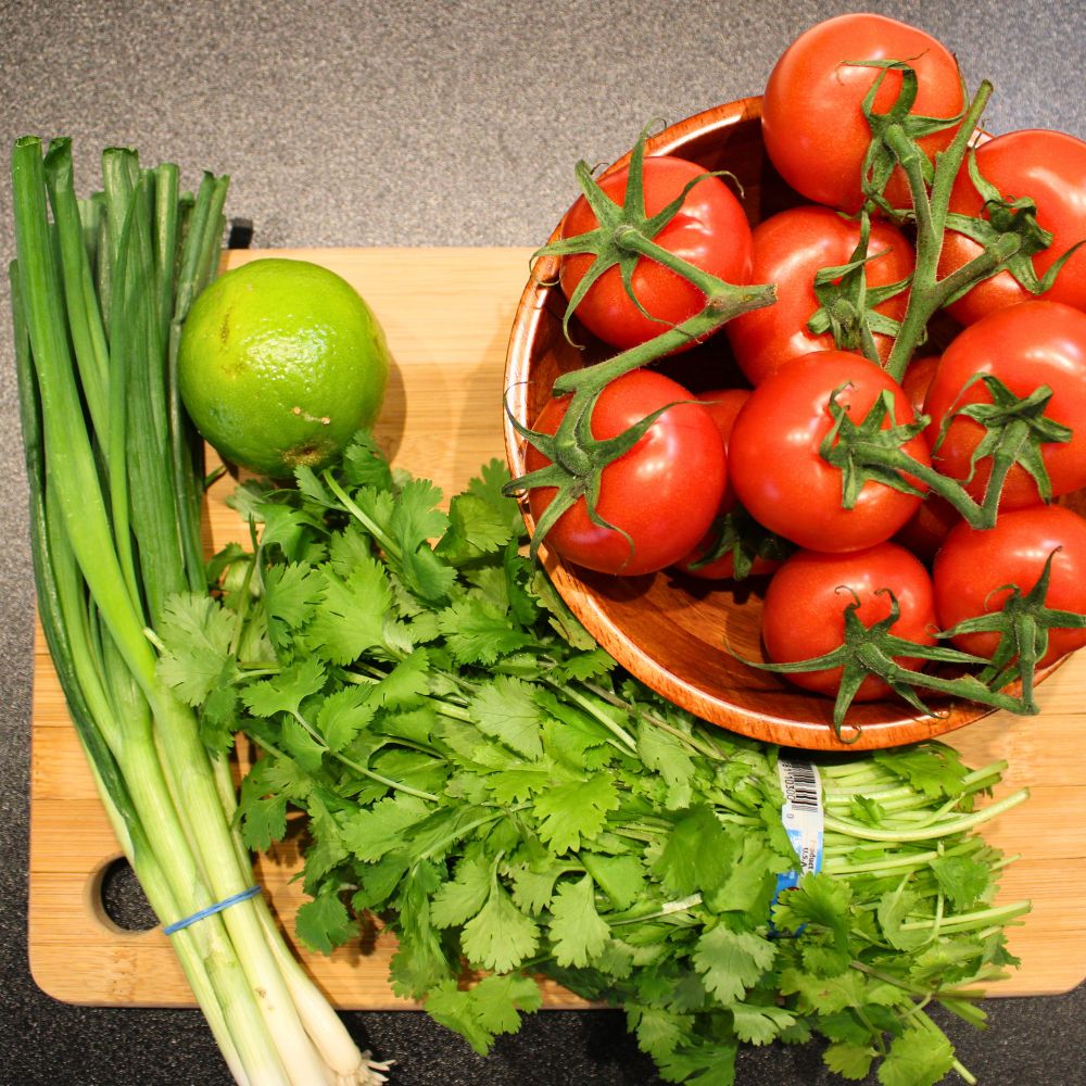 ingredients for restaurant style salsa: tomatoes on the vine, lime, bunch of cilantro, and green onion stalks on a cutting board