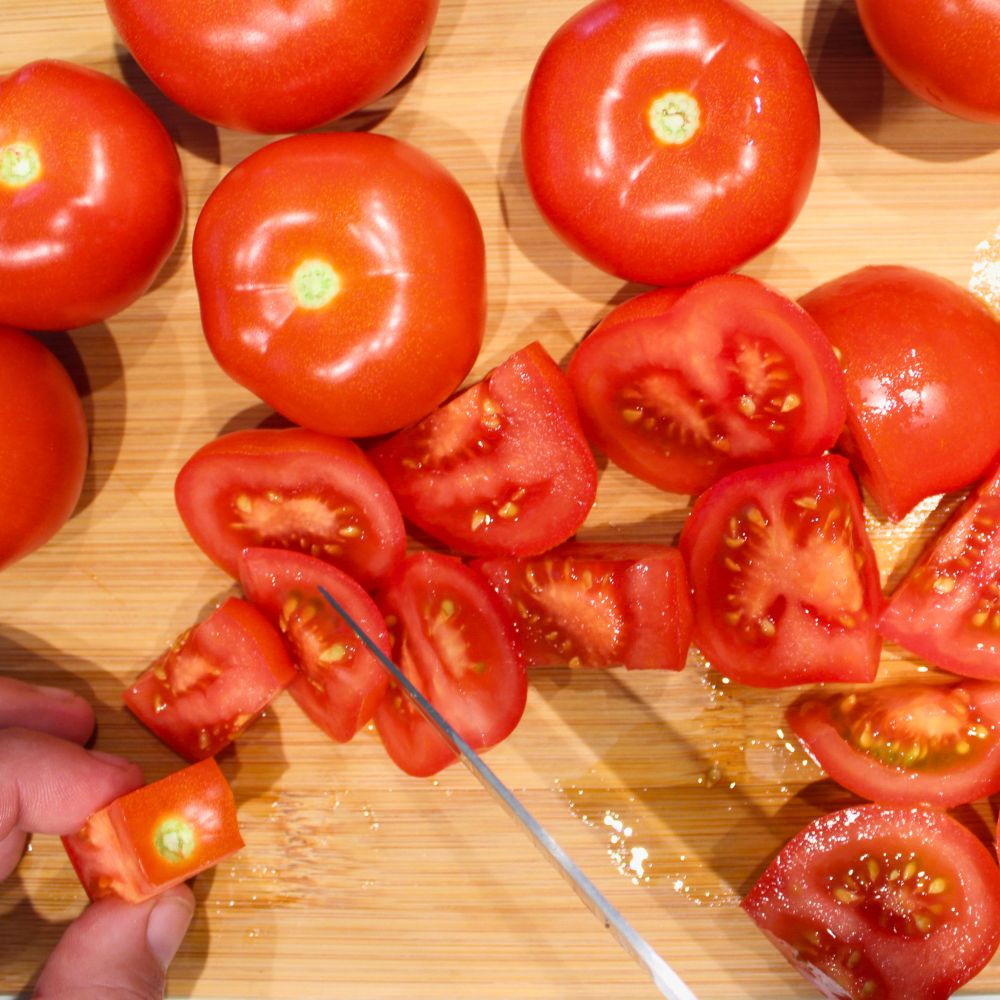 chopped tomatoes on a cutting board, with a hand holding a piece of tomato and a knife