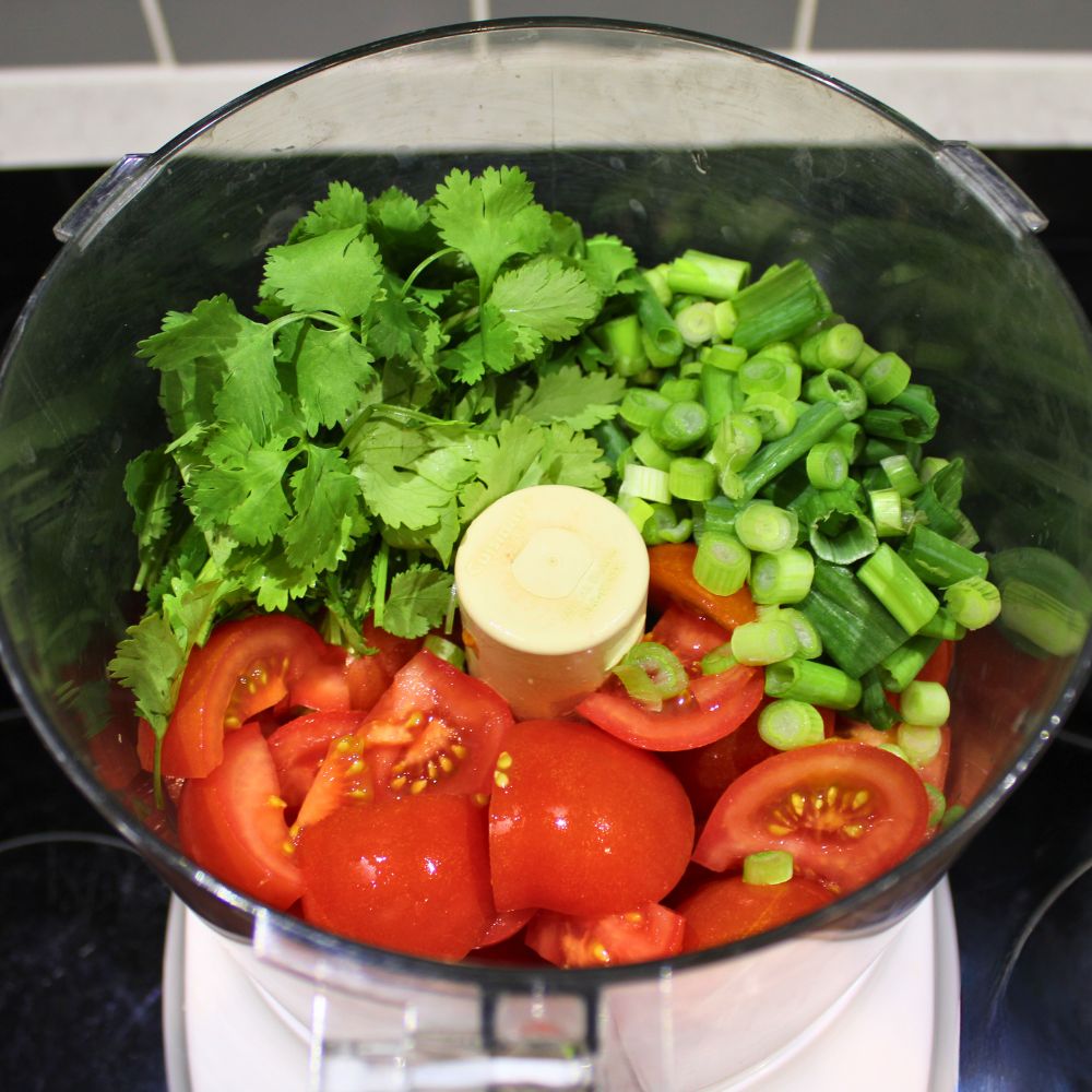 Ingredients for restaurant style salsa in a food processor, including chopped tomatoes, cilantro, and green onions