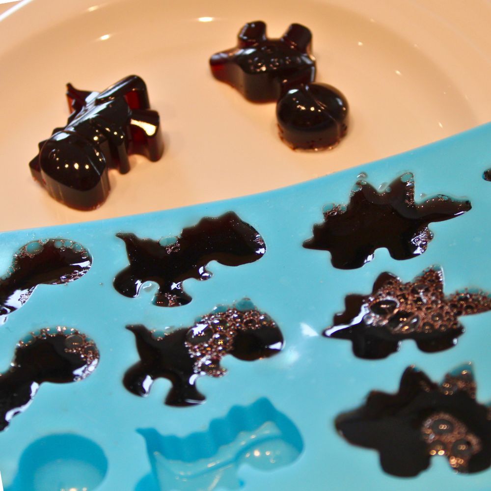 dinosaur shaped homemade gummies  in a silicone mold next to two gummy candies on a plate