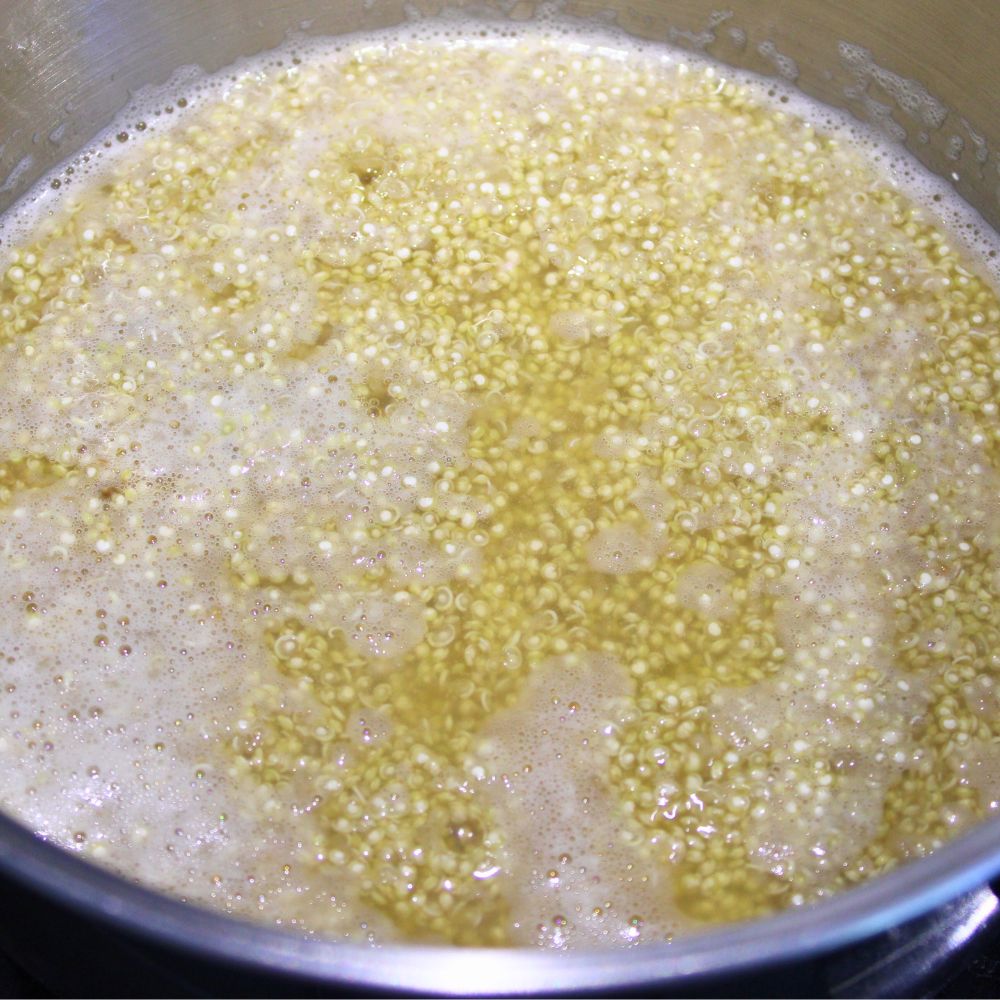 White quinoa and bone broth beginning to boil in a medium saucepan on a stove.