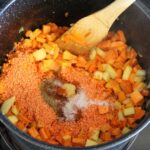 Red Lentil Sweet Potato Soup contents in a pot with a wooden spoon