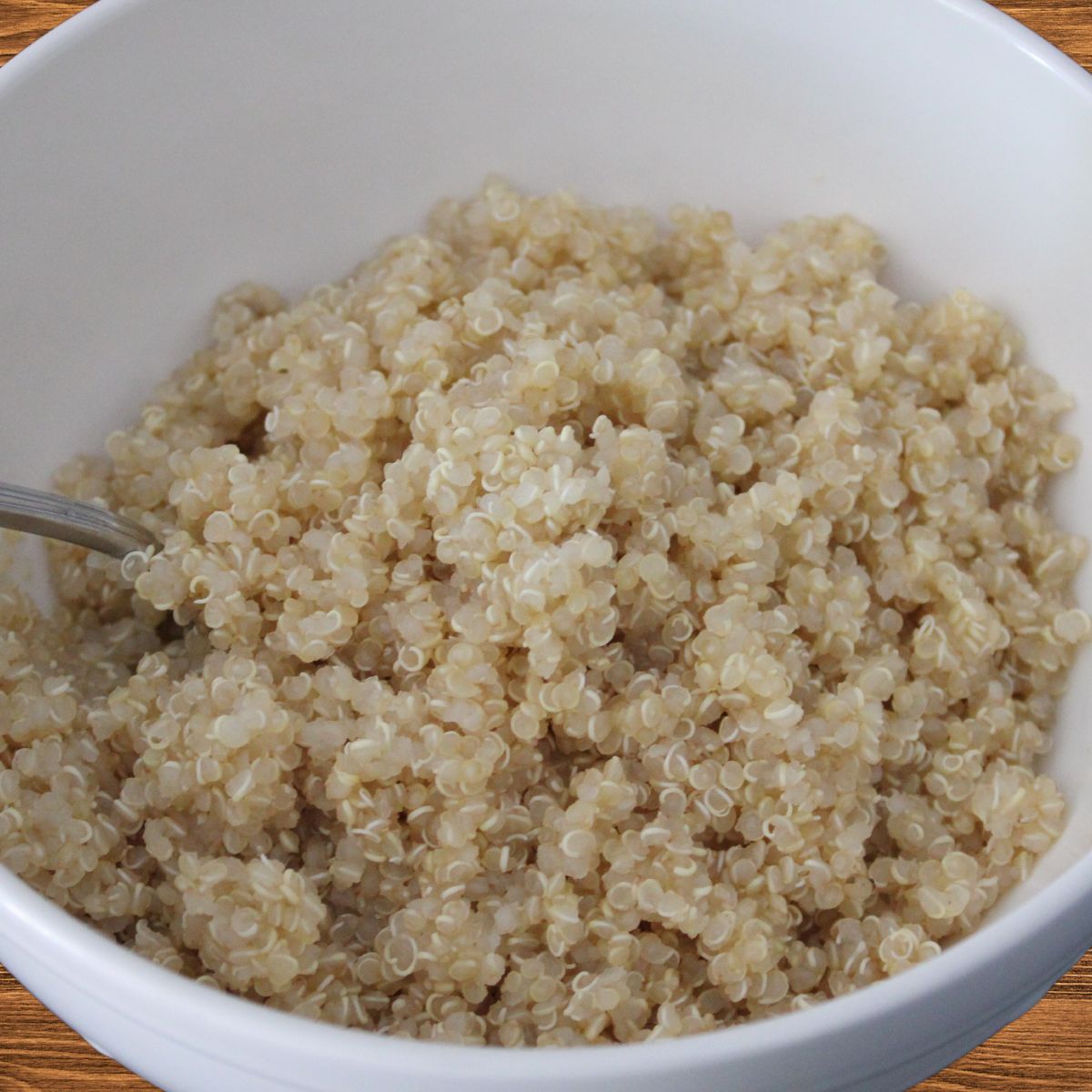 A bowl of cooked white quinoa, showcasing its fluffy texture, served with a spoon in a white bowl against a black background.