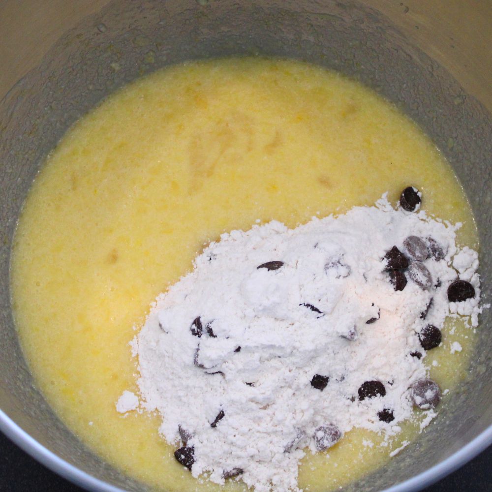 melted butter and eggs in a mixing bowl with flour and chocolate chips poured on top