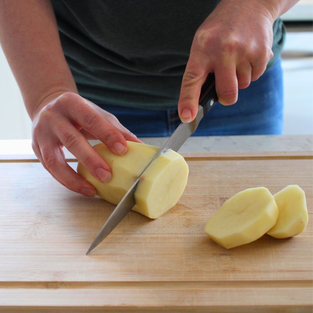 woman cutting a peeled potato on a cutting board