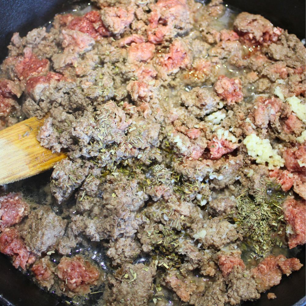 ground beef cooking in a pan, with a wooden spoon