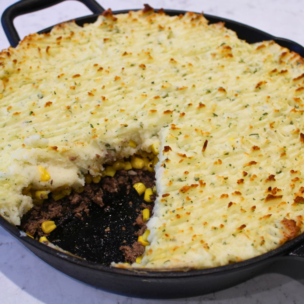 home made shepherds pie in a cast iron skillet with a slice removed so that the beef and corn filling are visible