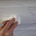 hand wiping crayon marks off a white kitchen cupboard