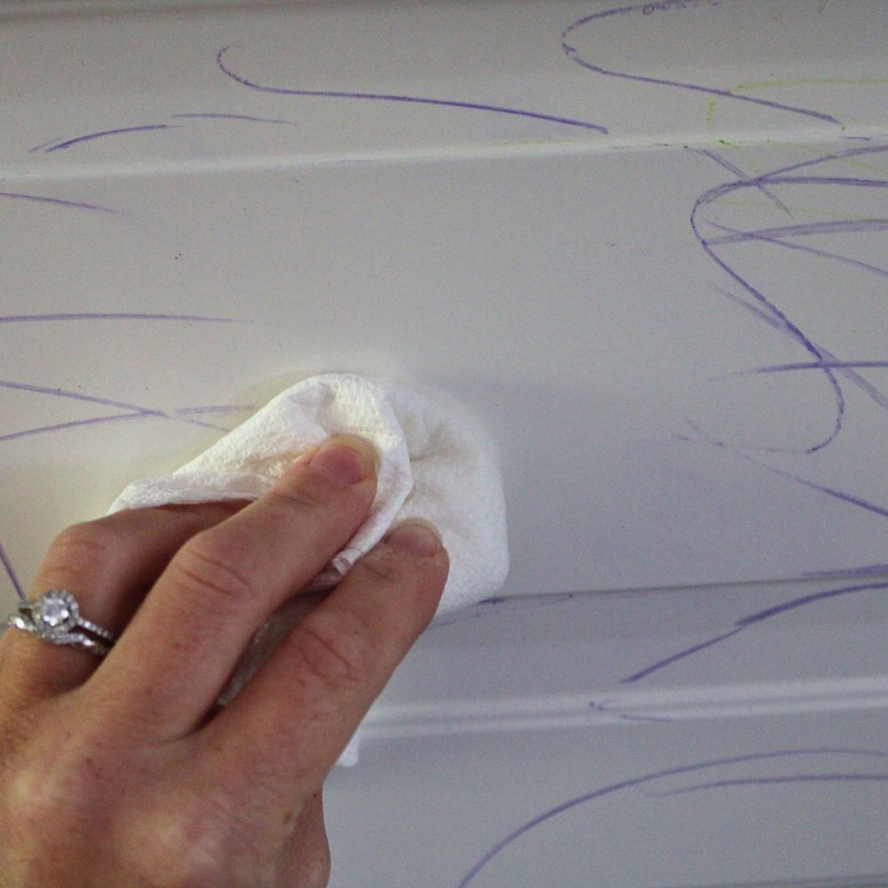 hand wiping crayon marks off a white kitchen cupboard