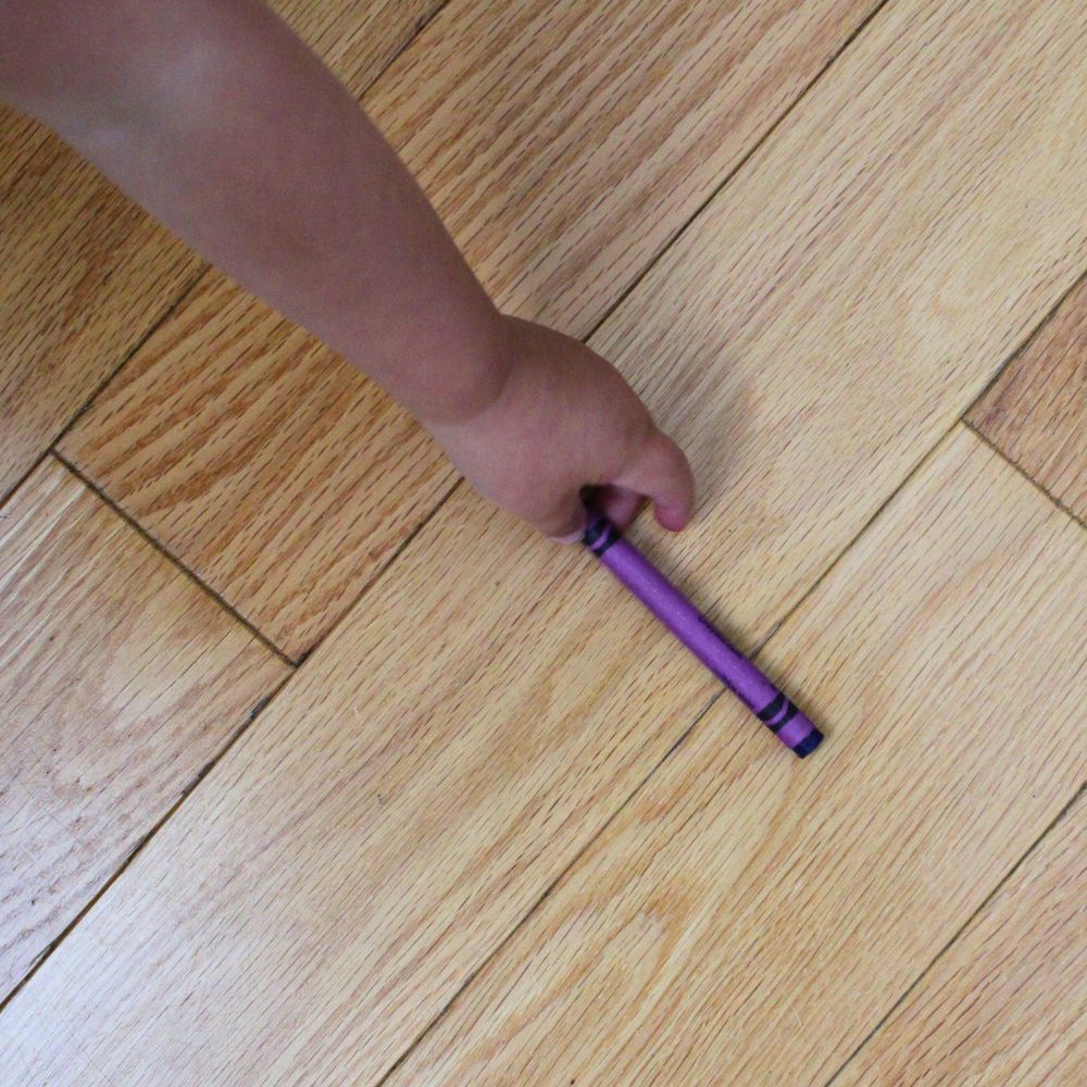 purple crayon on a hardwood floor, with a child's arm reaching for it