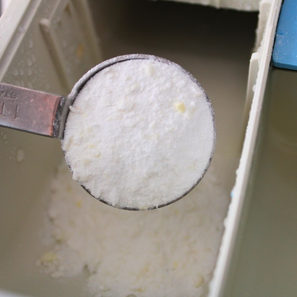 metal tablespoon pouring homemade powder laundry detergent into the main wash compartment of a laundry machine