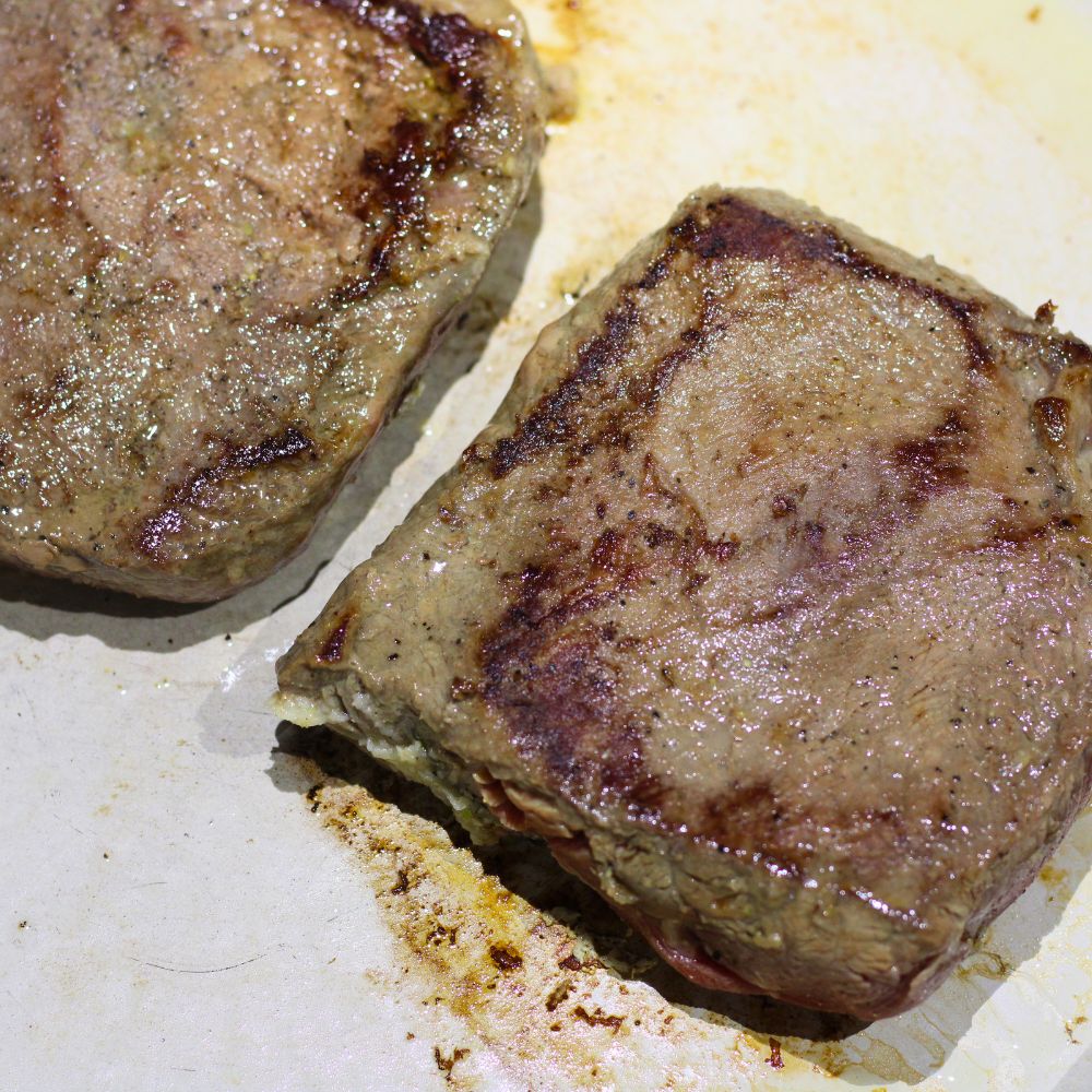 Two seasoned steaks with golden-brown sear marks cooking in an enameled cast iron pan. 