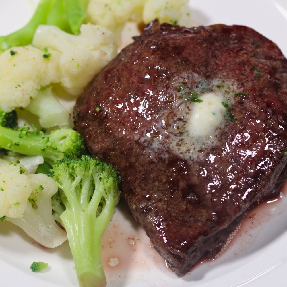 Plate of juicy cast iron oven-baked steak served with steamed broccoli and cauliflower.